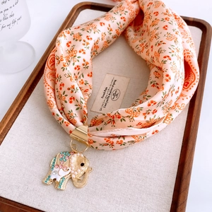 Détail d'un foulard en soie fleurie avec un pendentif éléphant doré orné de strass