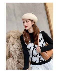 Outdoor street style showing beige wool beret hat paired with geometric knit vest