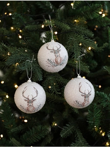 Close-up of white glitter Christmas balls with reindeer prints hanging on a green tree