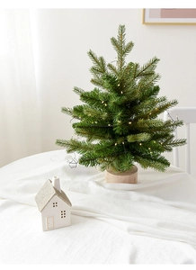 Mini PE Christmas tree with warm LED lights and a natural round wooden base on a white desk