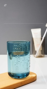 Blue translucent PS plastic mouthwash cup with water droplets on a wooden base