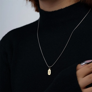 Collana minimalista dorata con ciondolo lettera X su catena snake su maglione nero