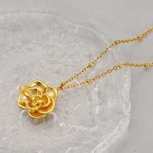 18K gold plated stainless steel rose flower pendant necklace on a textured glass plate