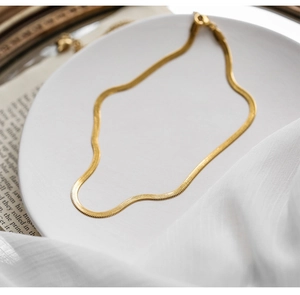 Detailed view of the gold flat snake chain necklace on a white ceramic tray