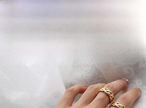 Detail shot of golden woven texture rings on fingers with a minimalist aesthetic
