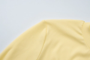 Gros plan sur la texture en maille côtelée et les coutures d'un haut jaune pâle