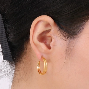 Close-up of golden C-shaped hoop earring with wheat ear texture on female model