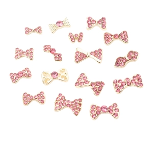 15-piece set of gold bow nail art charms with sparkling pink rhinestones on white background