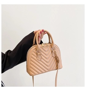 Detail of beige shell bag with V-shaped quilting, dual handles and golden hardware