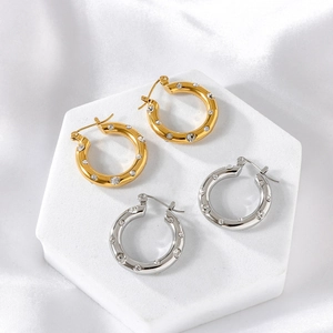 Detailed view of polished gold and silver hoop earrings with crystals on white silk