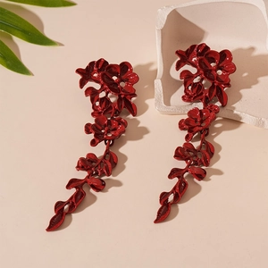 Detailed macro view of long red enamel floral tassel earrings on a neutral stone background