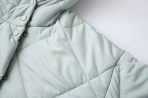 Close-up of mint blue quilted puffer coat showing snap buttons and fine stitching