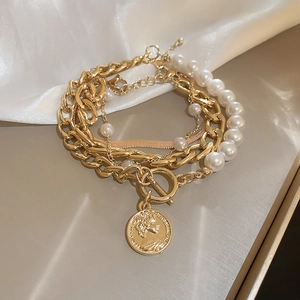Detail of layered gold metal chain with pearl bracelet and coin pendant on silk