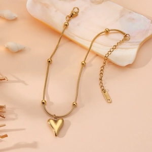 Détail du collier cœur en acier inoxydable doré avec perles sur fond rose doux