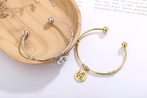 Detail of gold and silver open bangles with LOVE engraved charms on a wooden tray