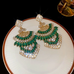 Detailed close-up of vintage gold earrings with green gems and rhinestones on a ceramic dish