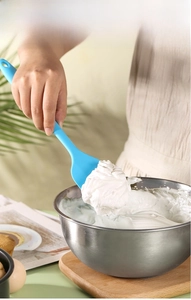 Light blue silicone spatula stirring cream in a stainless steel bowl for baking cakes