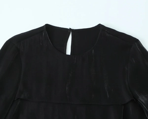 Detailed close-up of a black satin blouse featuring a round neck and back button closure