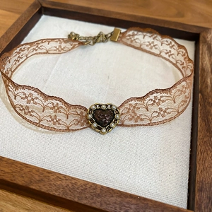 Detailed macro view of vintage lace choker with a bronze heart pendant in a wooden frame