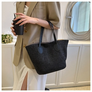 Detail of the black woven straw texture and leather strap on a large beach tote bag