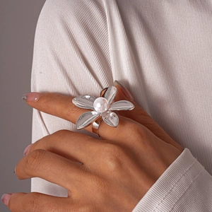 Detailed close-up of a large silver floral ring with a central pearl on finger