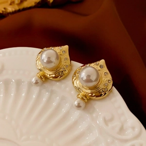 Detail von Vintage-Goldohrringen mit Perlen und Strasssteinen auf weißem Keramiktablett