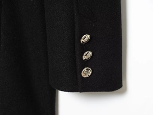 Close-up of black wool blend coat sleeve featuring three ornate gold embossed buttons