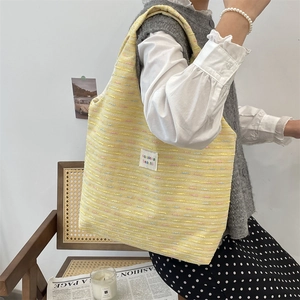 Yellow woven tweed tote bag with logo patch shown in a cozy lifestyle scene