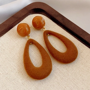 Brown flocked teardrop earrings in autumn style displayed on a beige linen surface