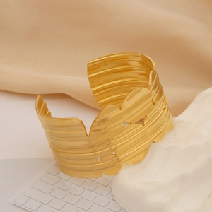 Close-up of golden hollowed-out wide cuff bracelet with textured hammer pattern detail