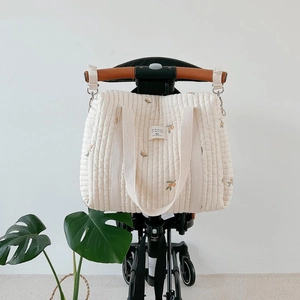 Quilted diaper bag with olive and lemon embroidery hanging on baby stroller straps