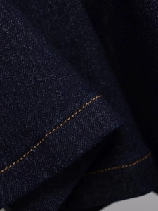 Close-up of dark blue denim fabric with precise gold-brown stitching and texture