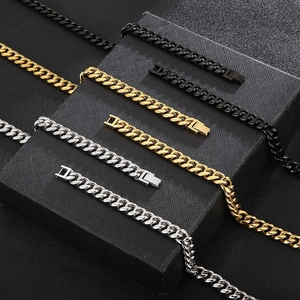 Three curb chain bracelets in black, gold, and silver finishes on a textured surface