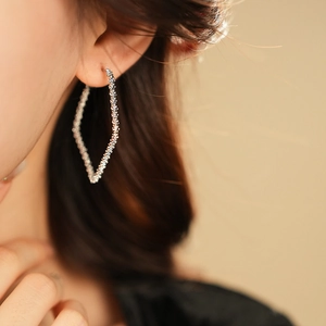 Macro shot of silver diamond-shaped hoop earrings with textured finish on model