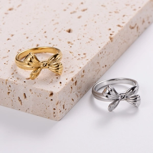 Classic minimalist bow rings in polished gold and silver on a marble stone display