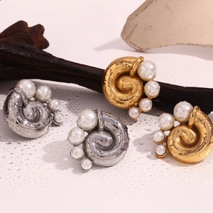 Macro detail of gold and silver spiral pearl earrings on a textured water-drop surface