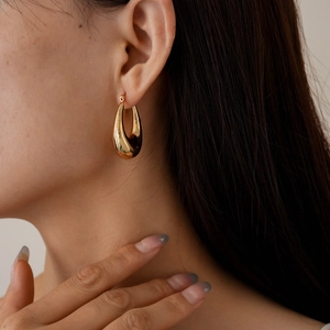 Primo piano di una modella con orecchini a goccia geometrici a U in metallo dorato