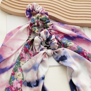 Detail view of two tie-dye floral silk scrunchies with long ribbons on a tray