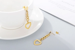Detailed close-up of hollow gold heart earrings with chain accents on white background