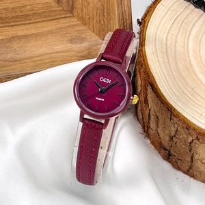 Montre minimaliste femme en cuir rouge foncé avec cadran doré sur un tissu blanc soyeux