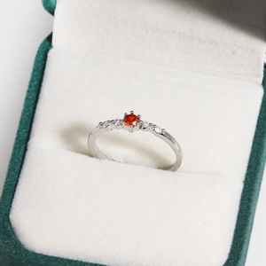 Detailed view of an orange zircon ring with white side stones in a green velvet jewelry box
