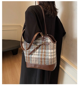 Detail of a large brown leather and plaid tweed tote bag shown on a model's shoulder
