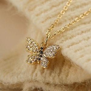Collana con ciondolo a farfalla dorata con zirconi chiari e neri su tessuto a maglia