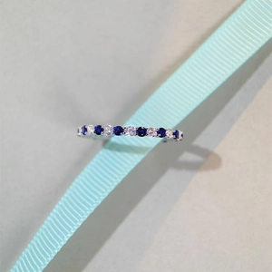 Macro shot of silver ring with blue and white round gems on light blue ribbon