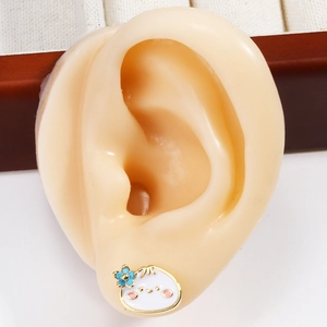Detailed view of a white enamel cartoon bun stud earring with a blue flower on ear model