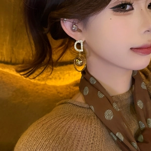 Detailed view of gold D-letter earrings with zircon accents on a female model
