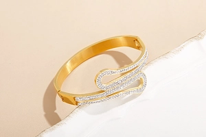 Macro detail of golden snake-shaped bracelet with rhinestones on a white ceramic plate