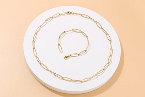 Detailed view of a gold shimmering oval link necklace and bracelet set on a white stand