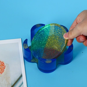 Detail of hand holding a colorful glitter resin coaster with a blue storage holder