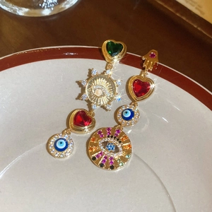 Detail of asymmetric vintage earrings with evil eye and heart charms on a ceramic plate